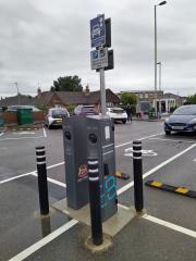 A signpost in a car park reading 'electric vehicle charging', with two electric vehicle charge points next to parking spaces.