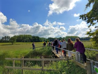 People walking over a bridge in a field on a summer's day